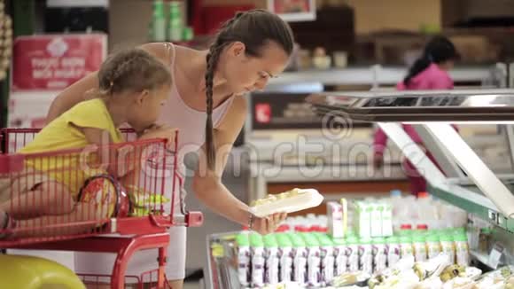 年轻的母亲带着女儿在手推车里挑选超市里的切水果视频的预览图