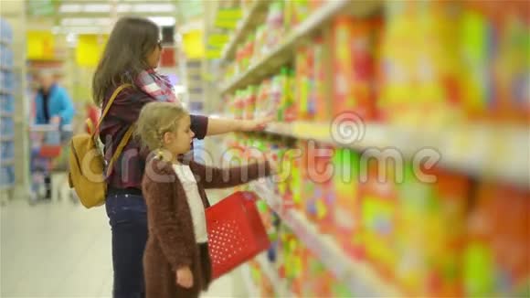 年轻的妻子和可爱的女孩站在货架附近的商品在超市妈妈和孩子一起在果汁店购物视频的预览图