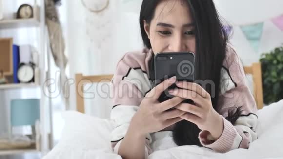 美丽的亚洲女孩用移动手机微笑的慢动作视频的预览图