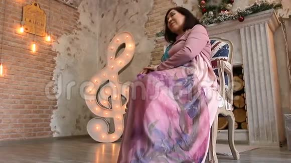 优雅的成年女人穿着紫丁香的连衣裙坐在椅子上奢华的室内视频的预览图