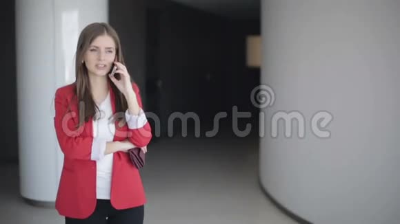 慢动作穿着红色夹克的女商人在办公室打电话视频的预览图