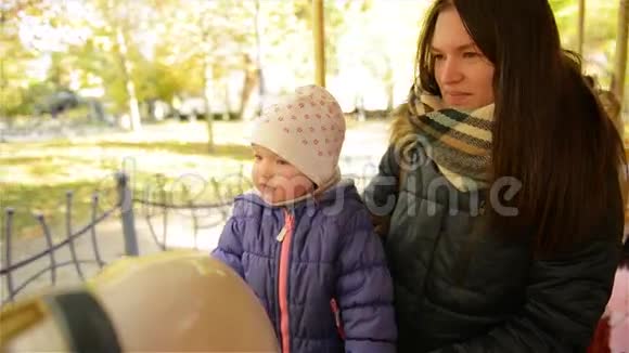 微笑母亲和孩子骑着旋转木马在秋天公园一天美丽的女人和可爱的女孩视频的预览图