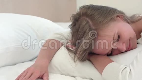 在家里或酒店房间睡在白床上的年轻金发女孩放松视频的预览图