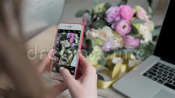 在花店里用智能手机带手机和笔记本电脑的花店里女性用手拍照美丽的花朵视频的预览图