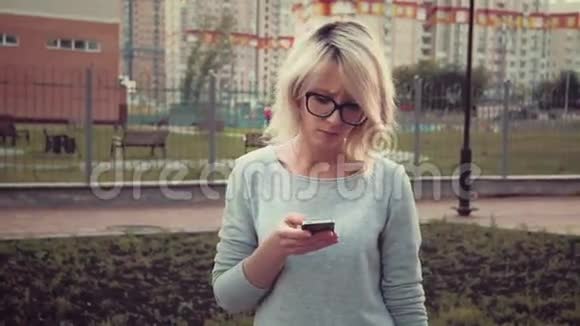 悲伤的年轻女子站在公园里的草坪上用她的智能手机发短信感到悲伤视频的预览图