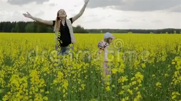 慢动作年轻的母女在春天开花的油菜田上跳舞视频的预览图