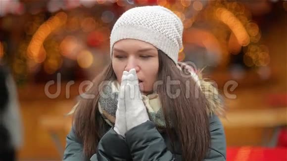 圣诞灯光背景下戴着白帽和灰色手套的笑女的肖像女人温暖的双手视频的预览图