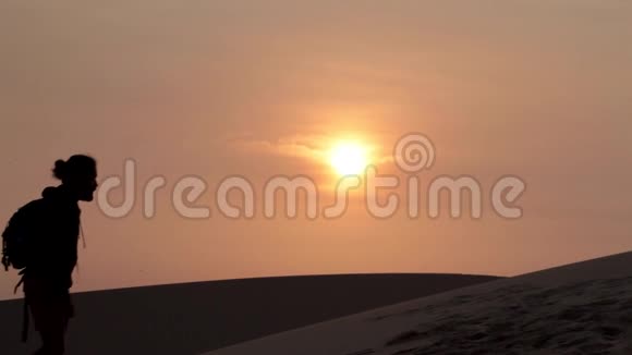 孤独的徒步旅行者日落时进入沙漠的剪影视频的预览图