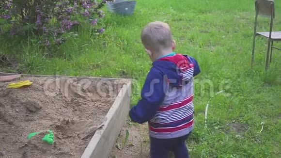 一个小男孩玩沙箱从运动鞋上擦沙子视频的预览图