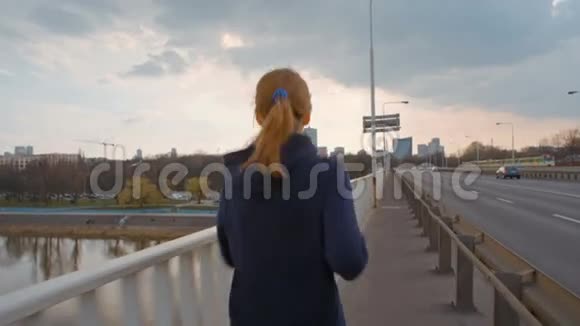 不错的年轻女士穿着运动服在城市的一座桥上奔跑的慢动作视频的预览图