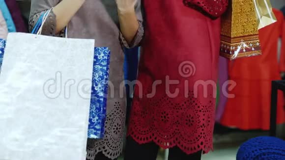 两个穿着带购物袋衣服的时髦女人站在商店里享受你的平板电脑微笑成功购物视频的预览图