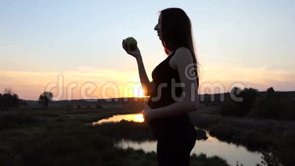 美丽的孕妇在日落时吃绿苹果视频的预览图