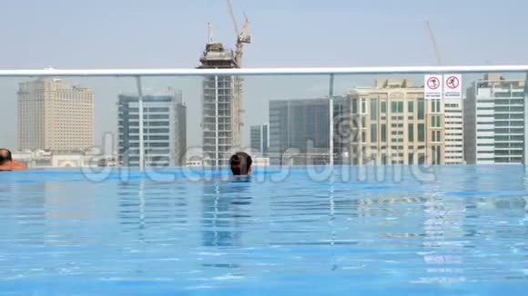女孩在屋顶的游泳池里放松在摩天大楼上可以看到城市景色视频的预览图