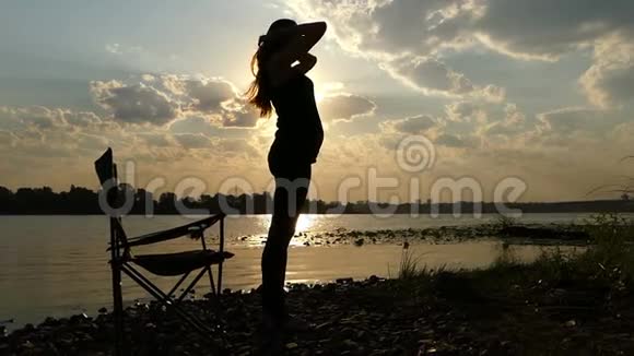 年轻的孕妇拍着肚子站在夕阳西下的河岸上视频的预览图