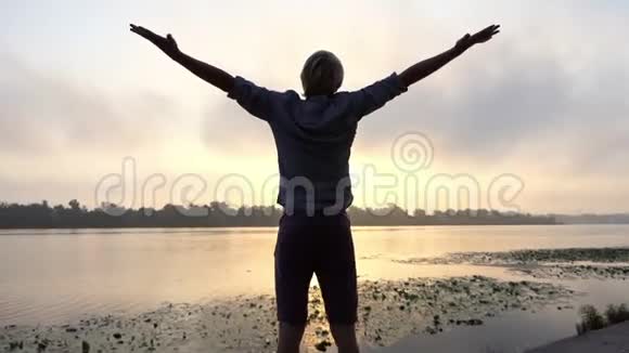 日落时分年轻人在风景如画的河岸上做呼吸运动视频的预览图
