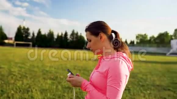 女人把耳机插到耳朵里准备在体育场跑步视频的预览图