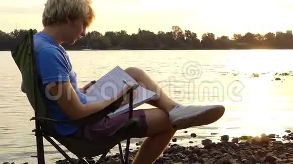 年轻人坐在河岸上做梦把一些东西写在记事本上视频的预览图