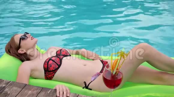 穿着泳衣五颜六色的鸡尾酒的女性在泳池里牵手穿着泳衣的漂亮年轻女性在床垫上漂浮视频的预览图