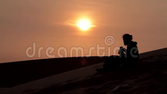 日落时分孤独的徒步旅行者坐在沙漠里喝着水视频的预览图