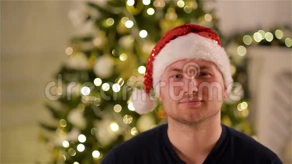 戴着圣诞帽的微笑帅哥看着圣诞树背景上的相机圣诞老人特写肖像视频的预览图