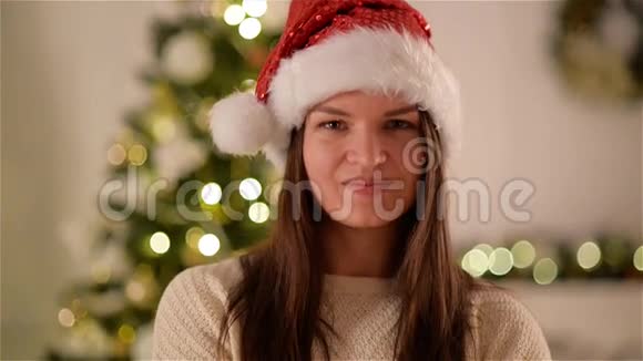 圣诞帽里的女孩在圣诞树背景上长着深色头发幸福和情感的女人微笑视频的预览图