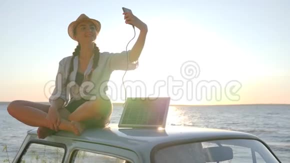 阳光下汽车自拍女孩坐在屋顶复古车背光做照片自拍手机视频的预览图