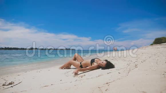 穿着黑色比基尼的黑发在夏天躺在海滩上在阳光下放松很适合年轻女孩视频的预览图