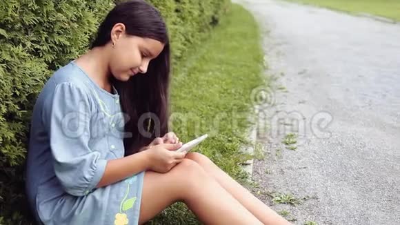 女孩坐在公园的草地上用平板电脑和微笑视频的预览图