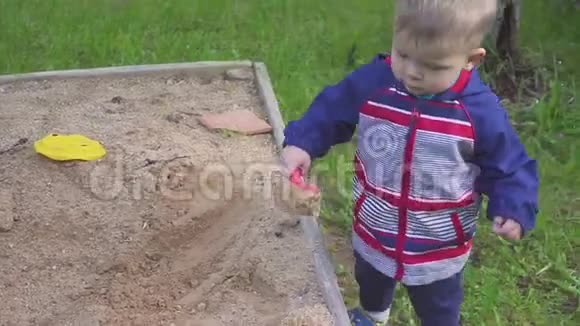 一个小男孩玩沙箱从运动鞋上擦沙子视频的预览图