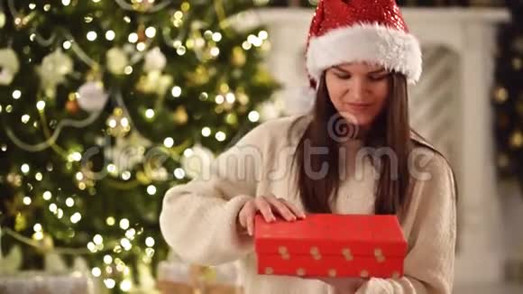 圣诞帽里快乐的女人手里拿着礼物打开它微笑长着深色头发的漂亮的布鲁内特视频的预览图