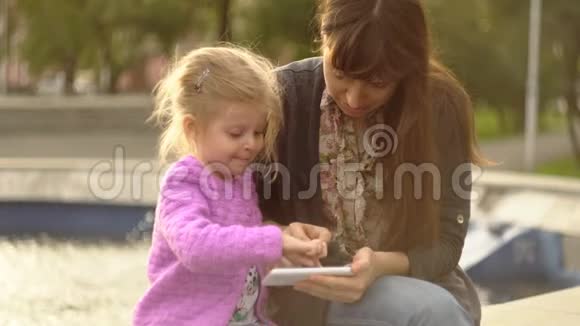妈妈和女儿在日落时在喷泉的电话里玩应用程序视频的预览图