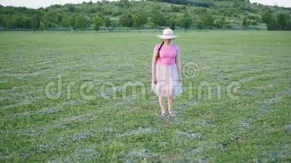 一个戴帽子的年轻女子走在绿色的田野上视频的预览图