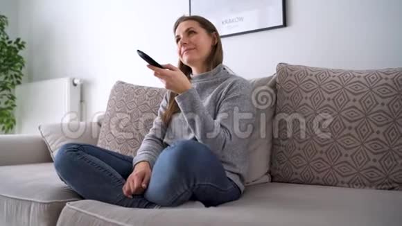 年轻女子躺在沙发上看电视她无限期地打开遥控器追踪镜头视频的预览图