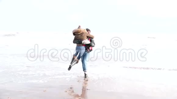 年轻夫妇在冬季海滩的波浪中奔跑视频的预览图