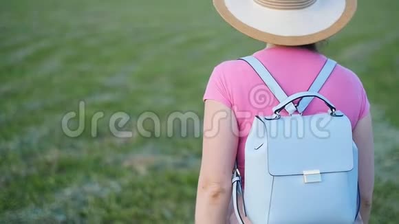 一个戴帽子的年轻女子走在绿色的田野上视频的预览图