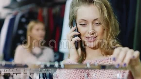 一个年轻女人在商店里选择一件衣服的肖像在手机上交谈视频的预览图