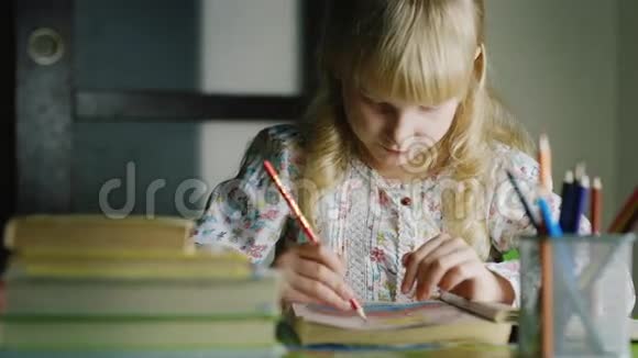 严肃的金发女孩在桌子旁画画在前景中一个花瓶和一叠书视频的预览图