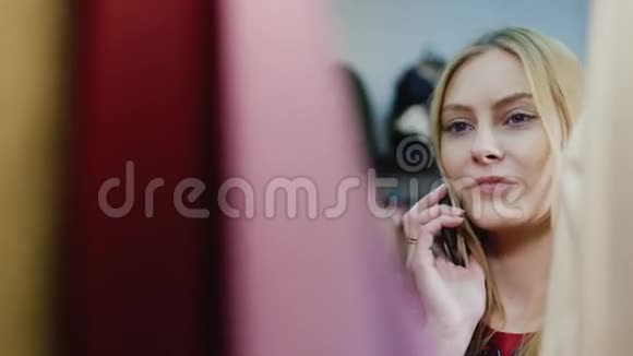 年轻的高加索女人在服装店打电话她看着衣架上的东西视频的预览图