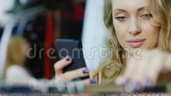 一个年轻女人在商店里挑选衣服的肖像享受智能手机视频的预览图