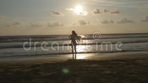 日落时分戴着围巾的年轻幸福的女人站在海边喜欢夏天的女孩比基尼女性剪影视频的预览图