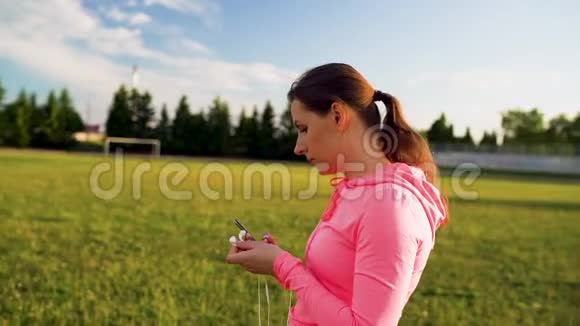 女人把耳机插到耳朵里准备在体育场跑步视频的预览图