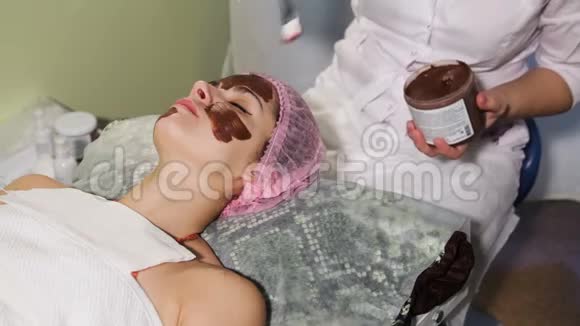 年轻漂亮的女人脸上有水疗程序巧克力温泉巧克力包装特写视频的预览图