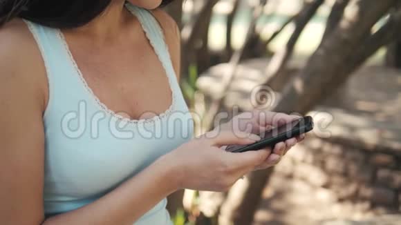 在阳光明媚的日子里一个聪明的女孩坐在长凳上的公园里网上购物的概念视频的预览图