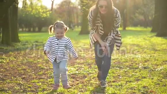 穿着条纹衣服的母亲和女儿正在一起玩耍享受公园里温暖的春天天气有趣的小女孩视频的预览图