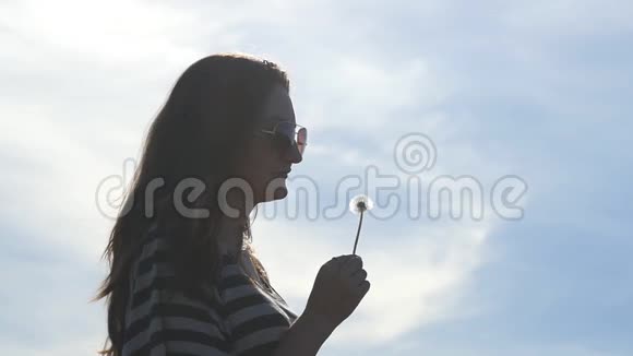 年轻的女人许愿在蓝天上吹蒲公英的种子背景是云慢动作概况视频的预览图