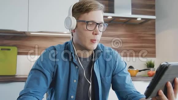 年轻的笑男看着数码平板电脑的流媒体电影戴着耳机吃麦片视频的预览图