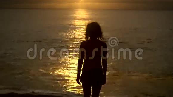 苗条的女孩在日落时慢慢地走进海洋来凉快太阳背景下年轻女子的剪影视频的预览图