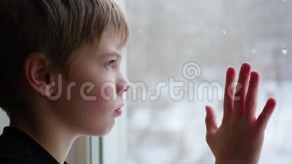 孩子坐在窗台上看着窗外的雪特写视频的预览图