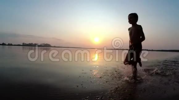 日落时快乐的孩子沿着海滩奔跑慢动作视频的预览图