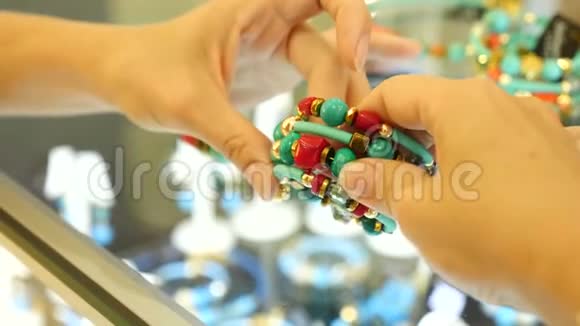 特写在珠宝店的柜台上女人的手拿着一个绿松石和珊瑚色的手镯4k慢动作视频的预览图